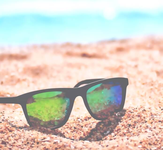 black-framed green-mirrored sunglasses on sandy beach